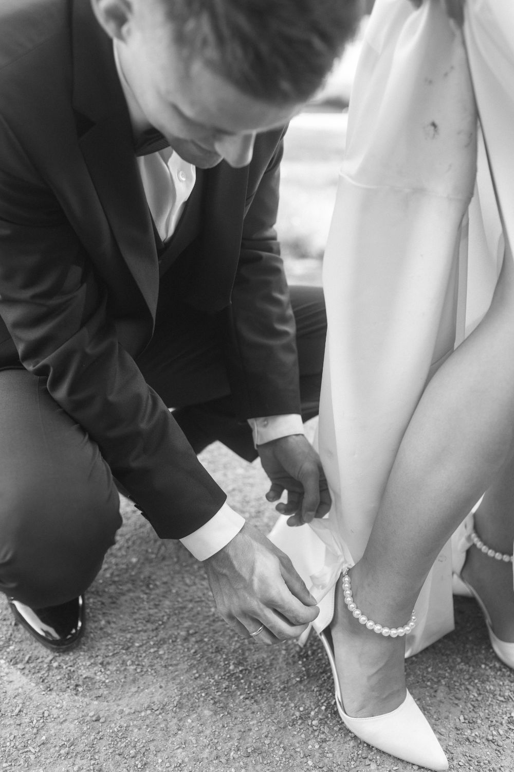 Groom assisting bride with bow on her wedding shoe strap.