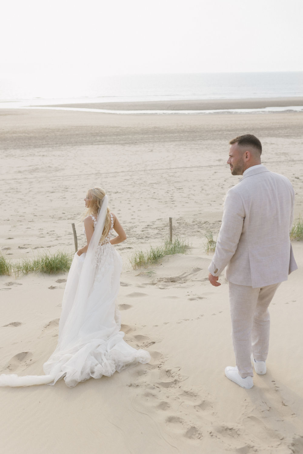 Bride and groom standing in Netherlands dunes by the sea.