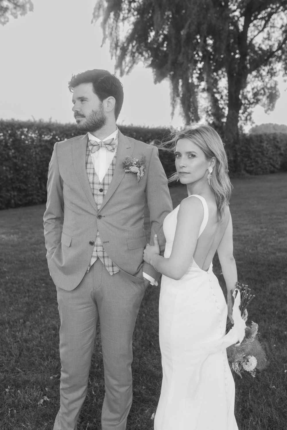 Flashy portrait of bride and groom; she looks at the camera, he gazes away, holding hands.