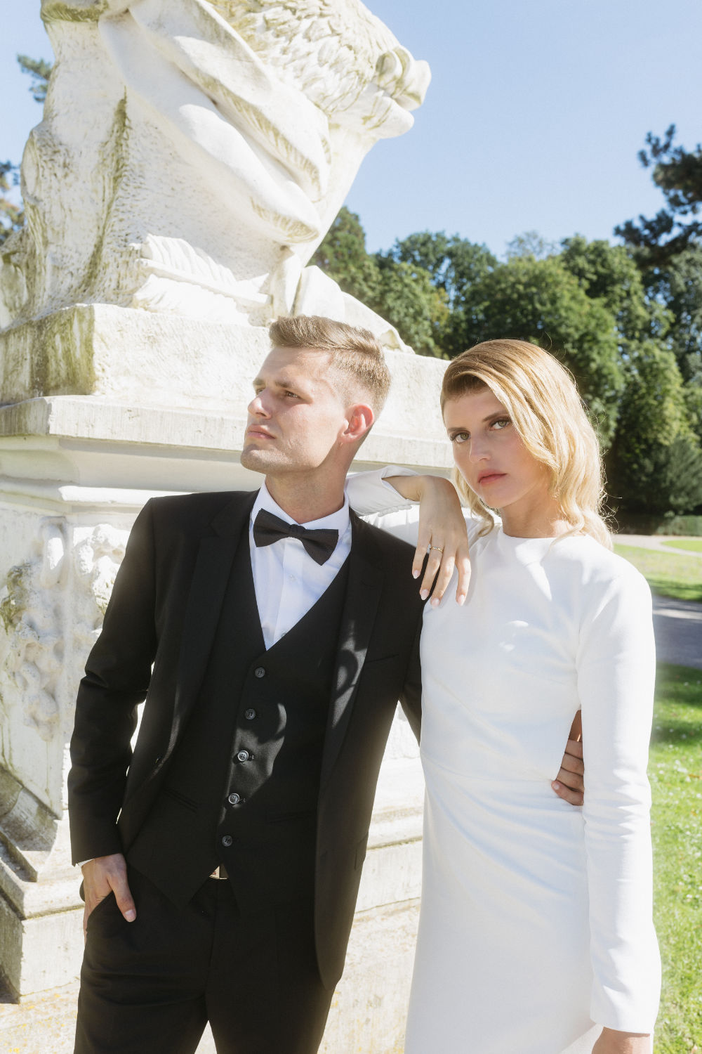 Bride and groom posing in front of a statue.