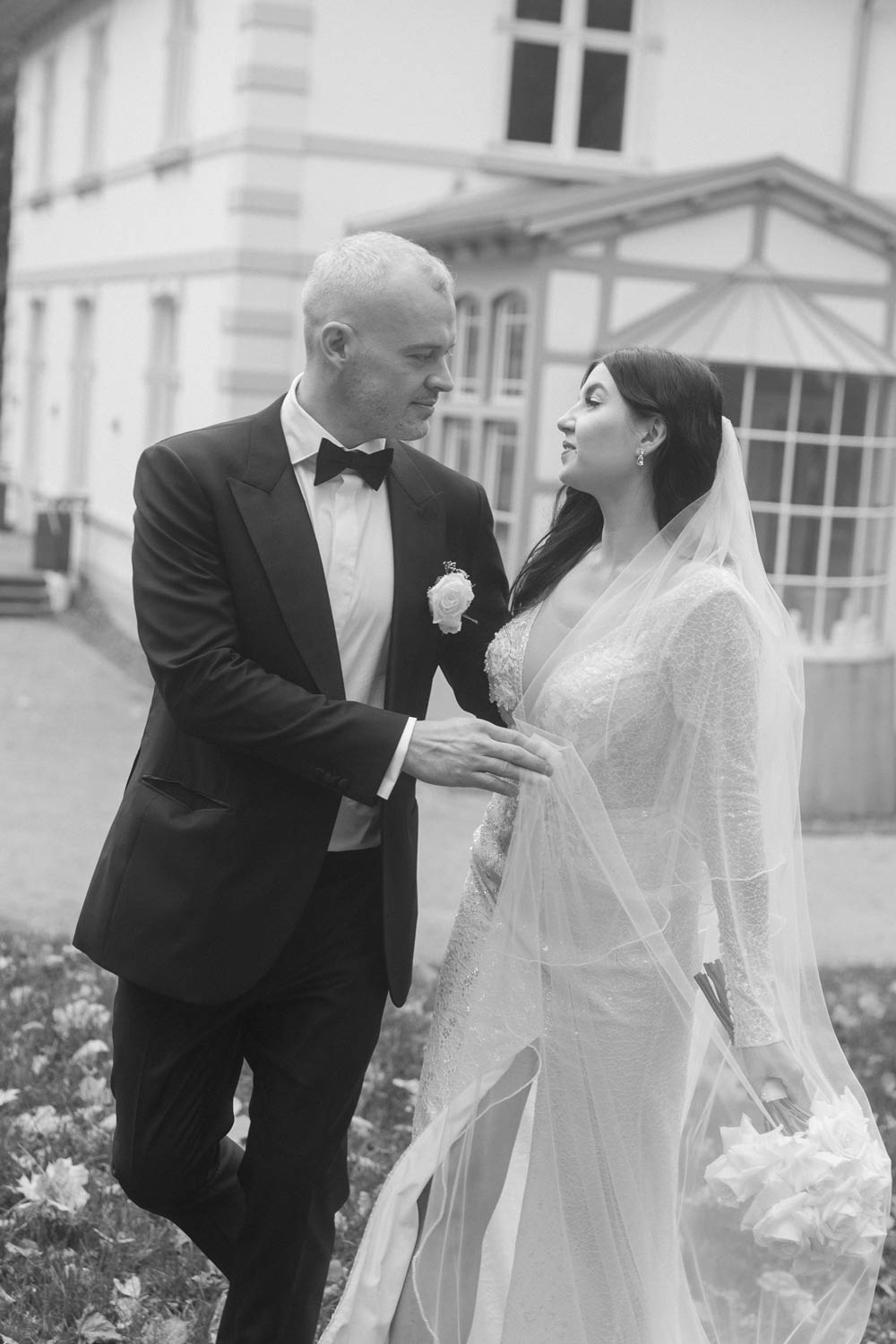 Bride and groom share a loving gaze in front of a villa.