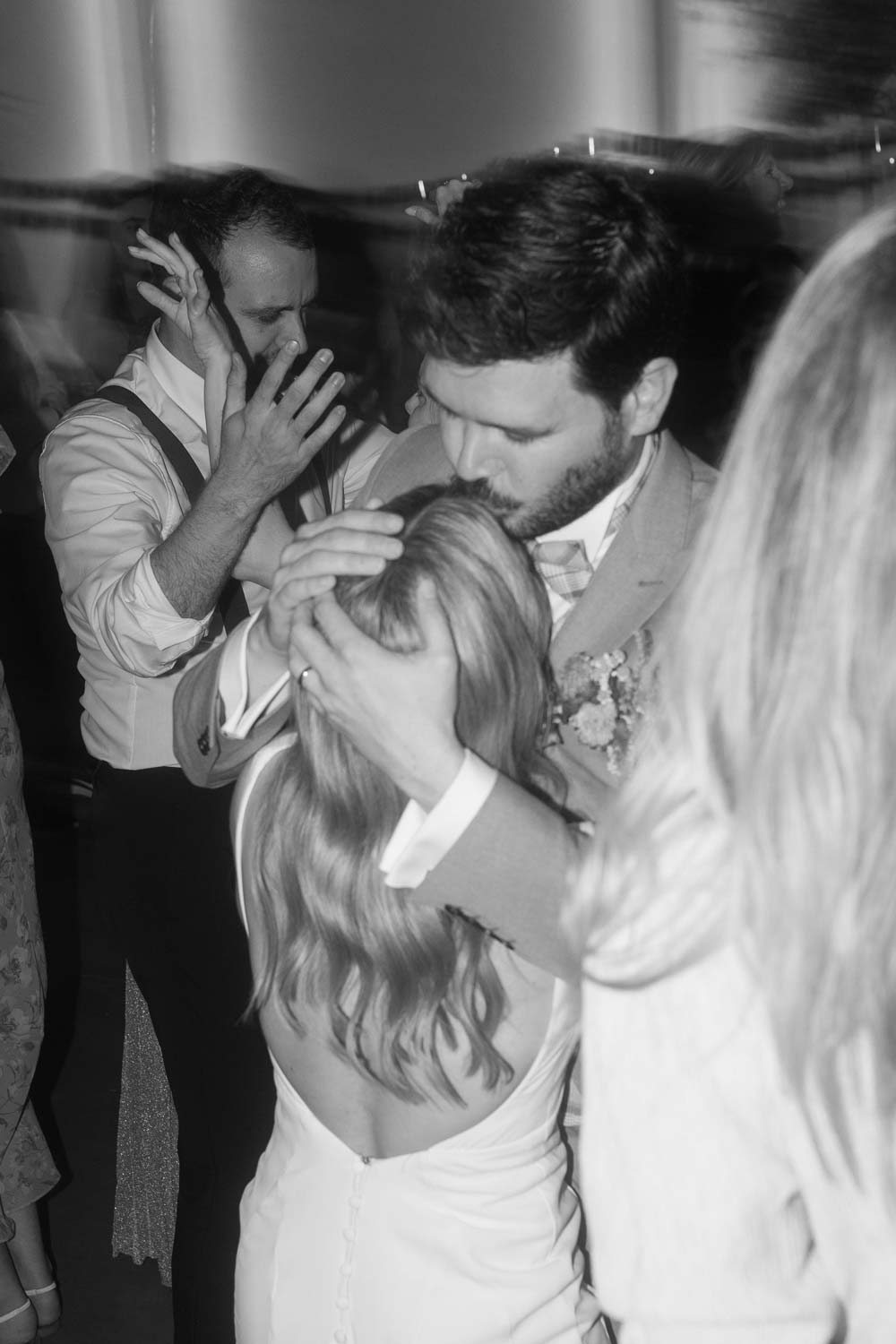 Groom kisses bride's forehead while dancing at their wedding party.