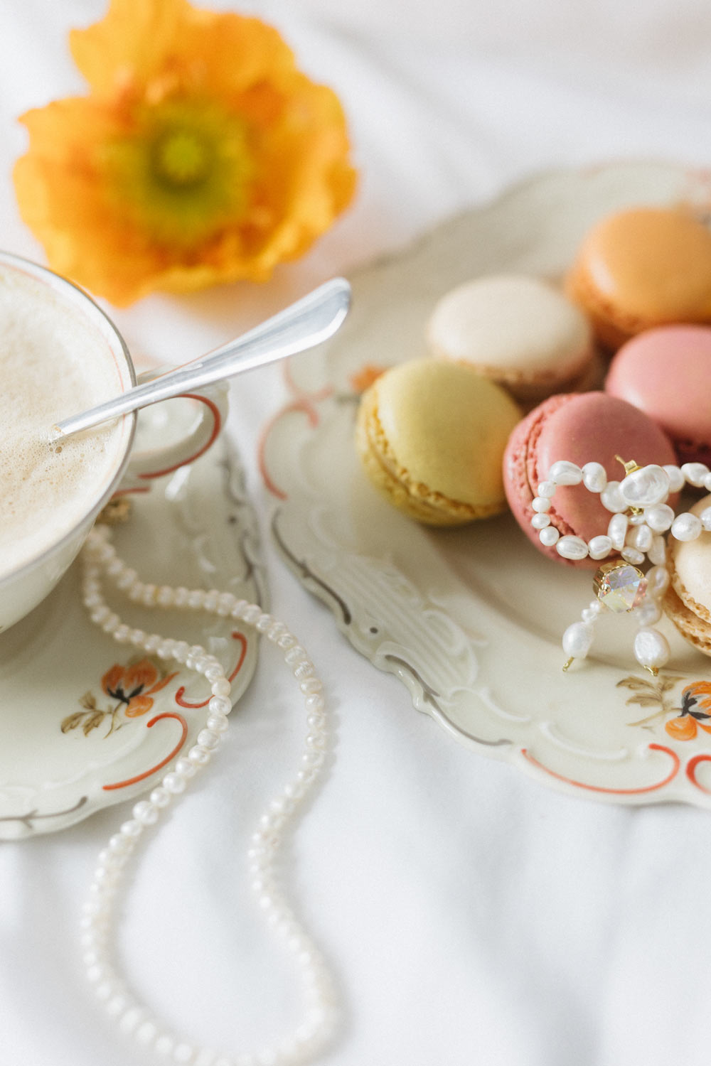 Coffee, macarons, and pearl jewellery displayed on vintage dishes.