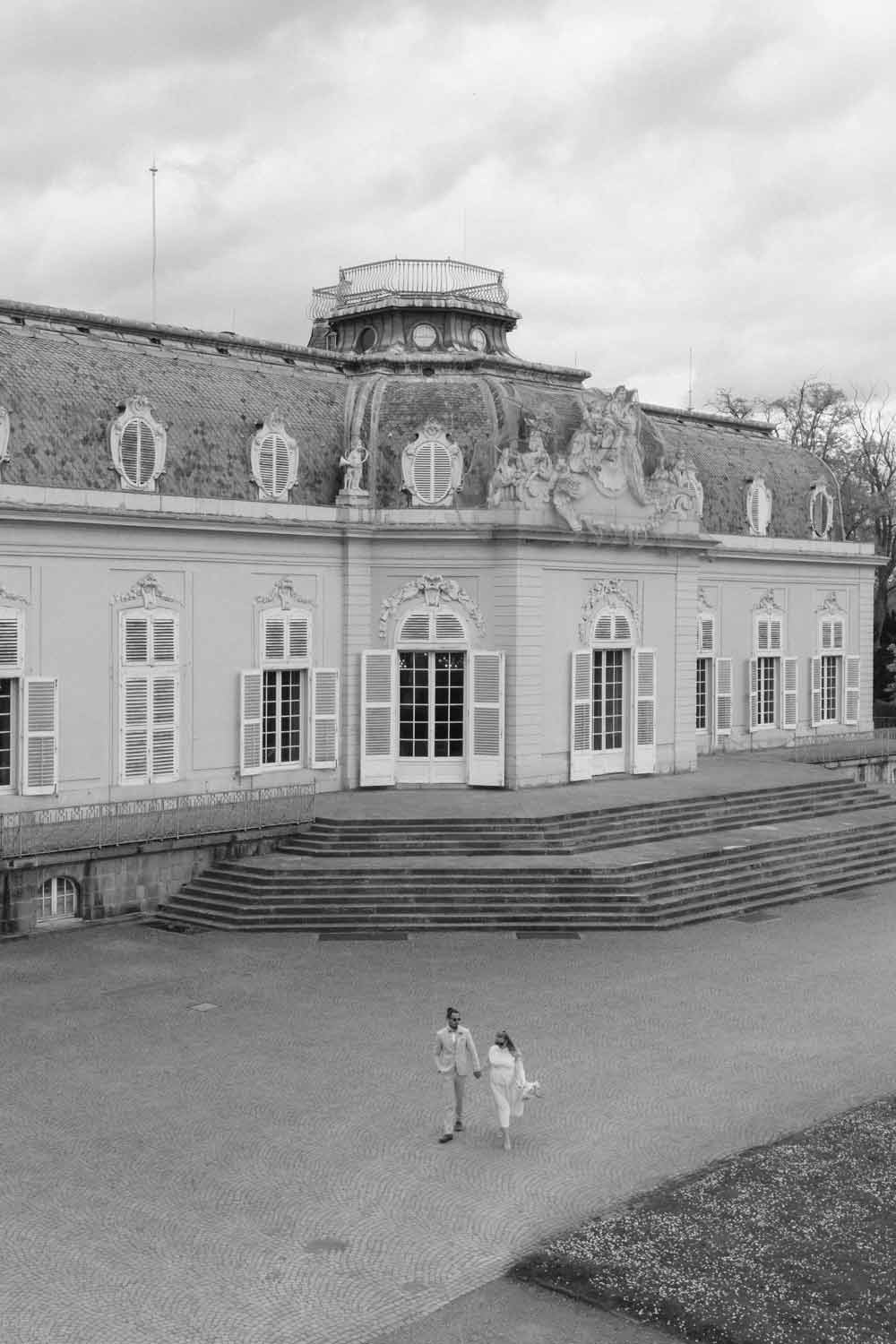 Bride and groom walk in front of a palace, captured from above with a drone.