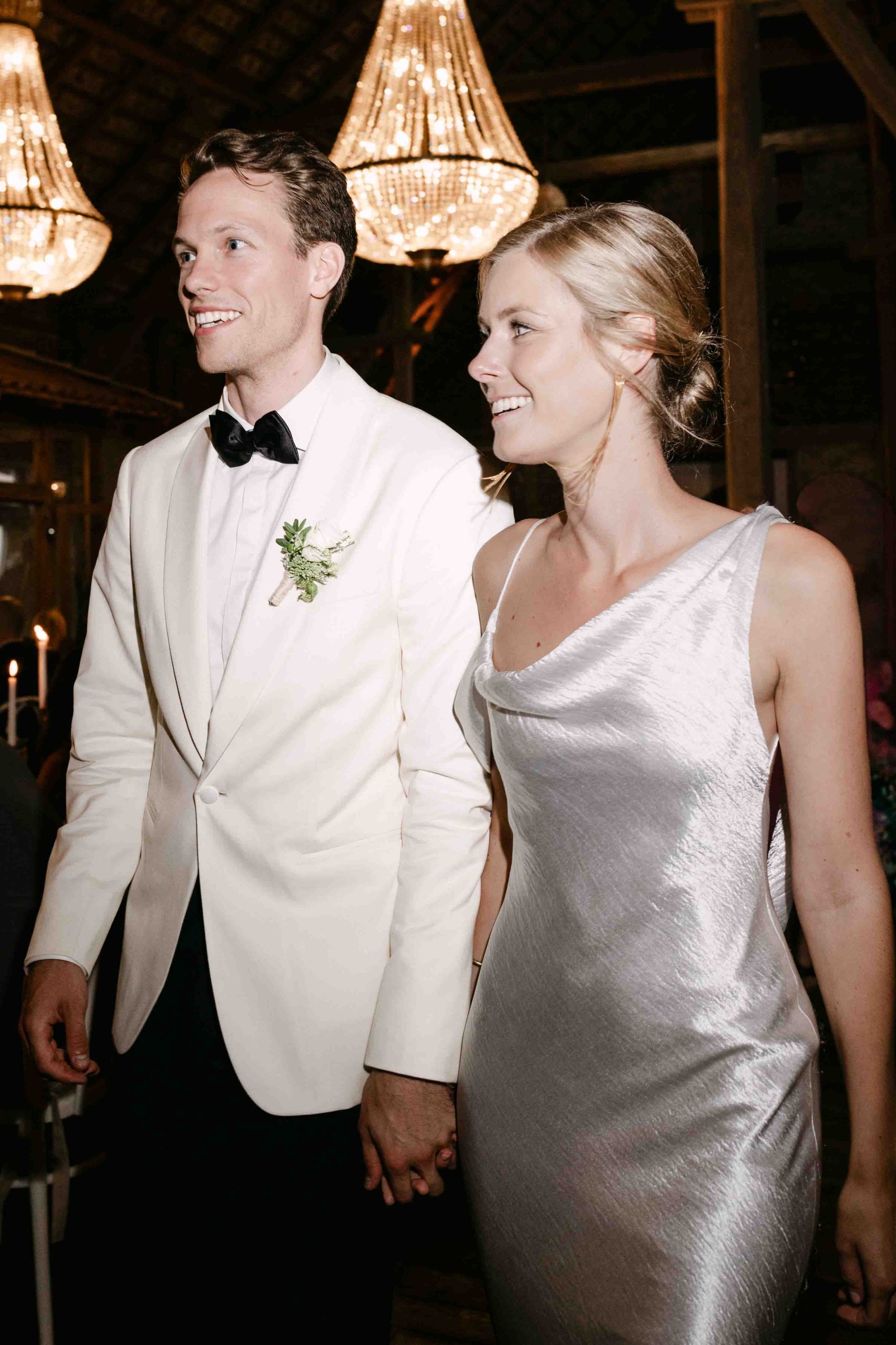 Bride and groom walking under chandeliers, captured mid-movement.  