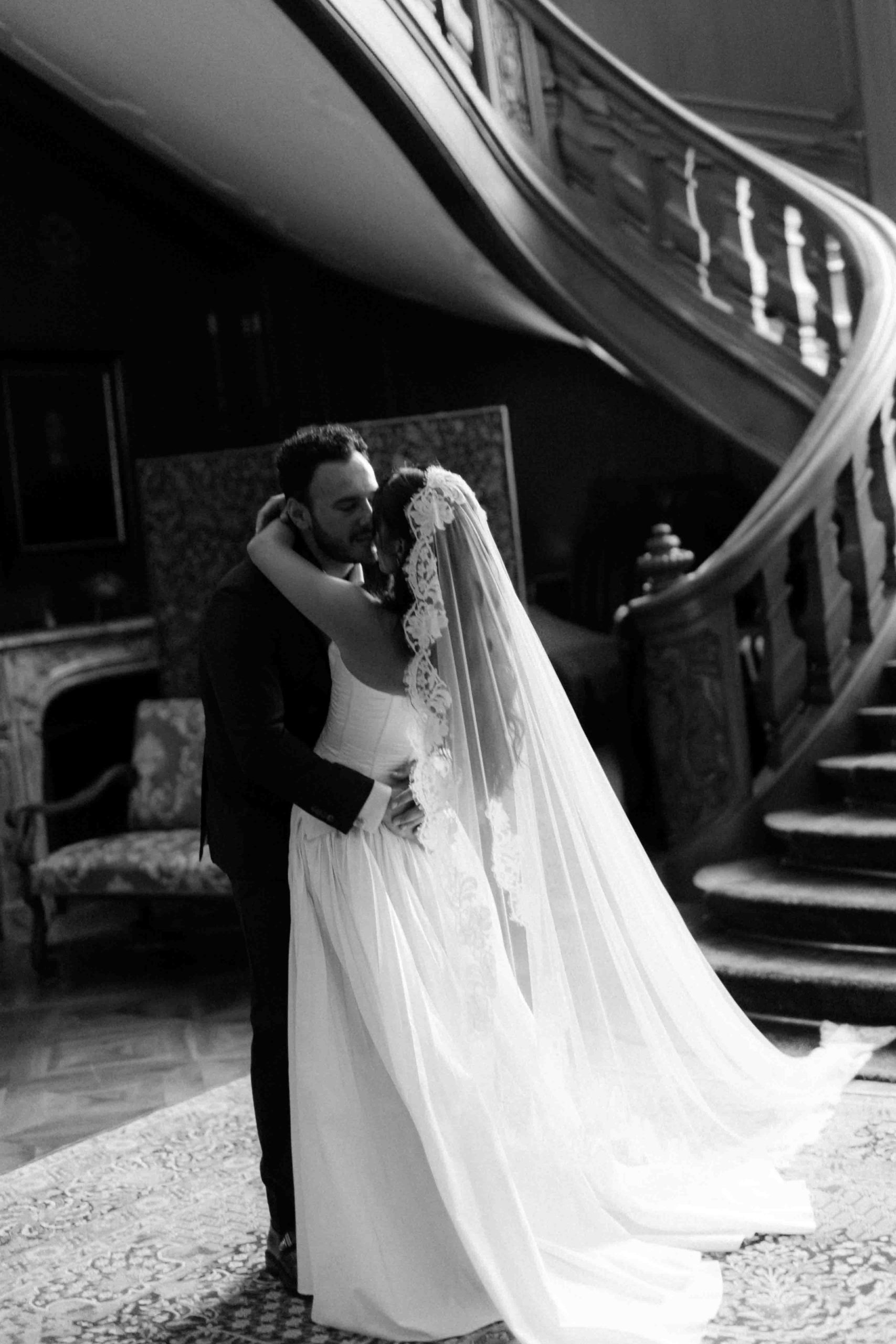 Bride and groom embracing in front of a staircase in black and white.